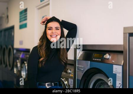 Porträt einer lächelnden jungen Frau, die in einem Waschsalon Wäsche macht Stockfoto