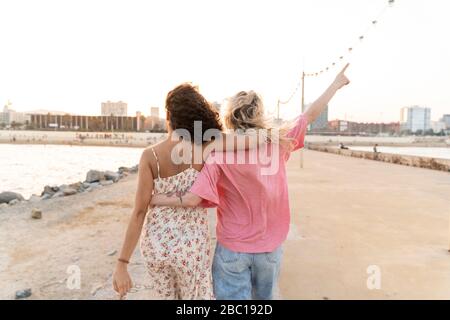 Rückansicht von zwei jungen Frauen an der Uferpromenade bei Sonnenuntergang Stockfoto