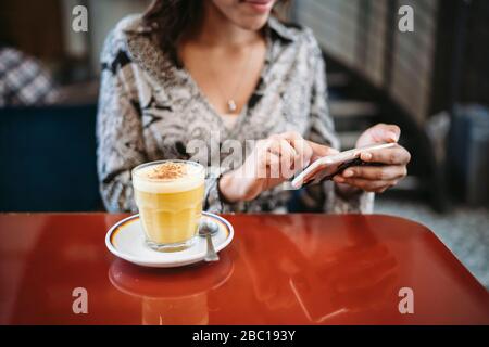 Junge Frau, die in einem Café hinter der Fensterscheibe einen Laptop benutzt Stockfoto