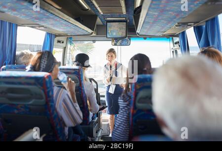 Weiblicher Reiseleiter mit Mikrofon, der mit aktiven Seniorentouristen im Reisebus spricht Stockfoto