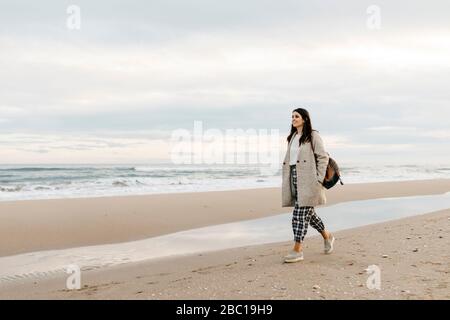 Junge Frau, die bei Sonnenuntergang an einem abgelegenen Strand spazieren geht Stockfoto