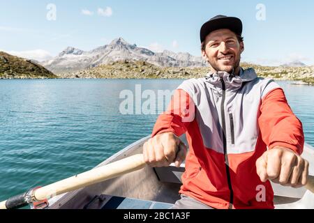 Junger lächelnder Mann in einem Ruderboot, Suretta See, Graubünden, Schweiz Stockfoto