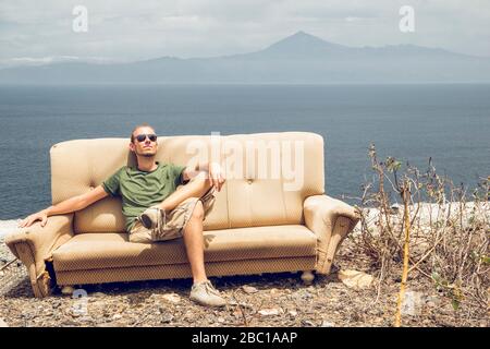 Junger Mann, der sich auf der gebrochenen Couch entspannt, die Sonne genießt, La Gomera, Spanien Stockfoto