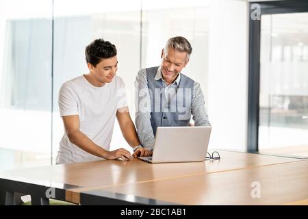 Leitender Geschäftsmann, der mit einem jungen Kollegen arbeitet und einen Laptop verwendet Stockfoto