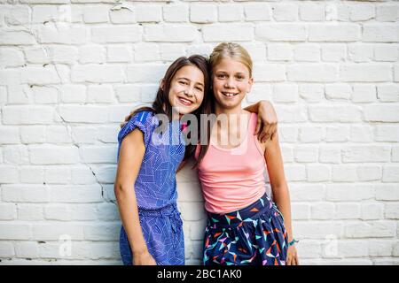 Porträt von zwei glücklichen Mädchen umarmt an einer Wand Stockfoto