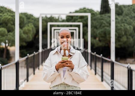 Porträt einer glücklichen Frau, die das Handy auf einer Brücke hält Stockfoto