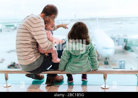 Vater mit zwei Töchtern, die vor einem Flugzeug am Flughafen sitzen Stockfoto