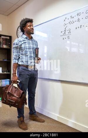 Mathelehrer mit seiner Tasche und seinem Mathebuch vor dem Whiteboard Stockfoto