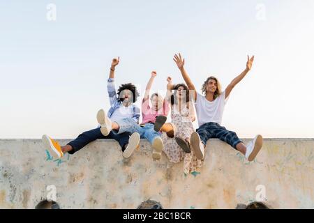 Porträt von glücklichen Freunden sitzen auf einer Betonwand im Freien Stockfoto