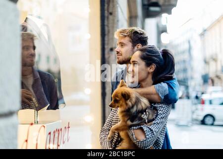 Junges Paar mit Hund, das in der Stadt im Schaufenster schaut Stockfoto