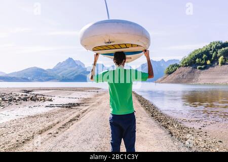 Mann, der SUP-Board zum See trägt Stockfoto