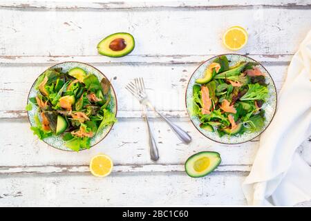 Zwei Teller mit verzehrfertigen grünen Salaten mit Rucola, Lollo Rosso-Salat, Babyspinat, Rote Bete Blätter, Avocado, Maissalat und Lachs Stockfoto