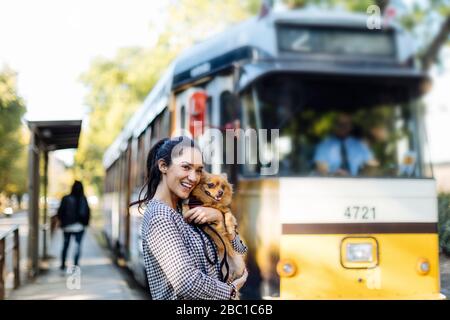 Glückliche junge Frau mit Hund an der Straßenbahnhaltestelle in der Stadt Stockfoto