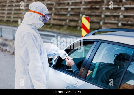 Mann, der Schutzkleidung trägt und den älteren Mann im Auto kontrolliert Stockfoto