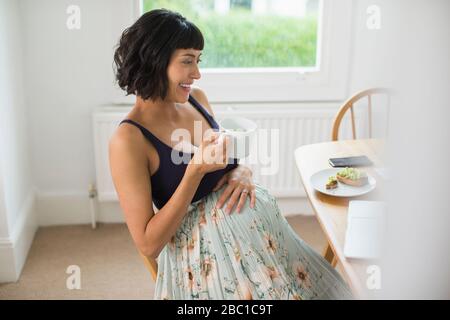 Glückliche schwangere Frau trinkt Tee am Laptop Stockfoto