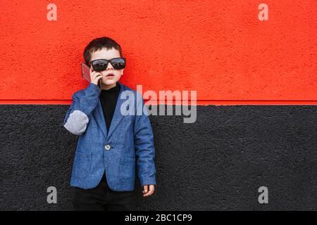 Porträt des kleinen Jungen am Telefon in Anzug Mantel und übergroße Sonnenbrille Stockfoto