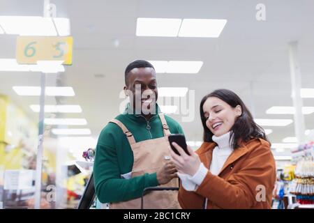 Lebensmittelhändler helfen Kunden mit Smartphone im Supermarkt Stockfoto