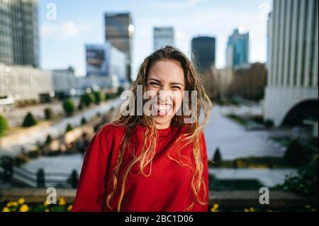 Porträt einer glücklichen jungen Frau in der Stadt, die ihre Zunge herausstreckt Stockfoto