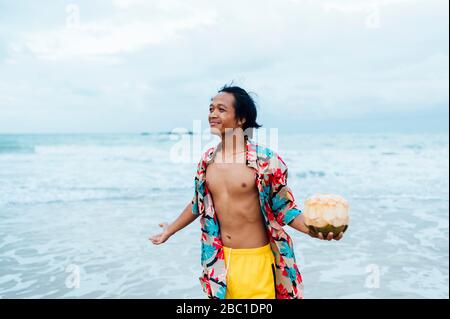 Porträt eines glücklichen Mannes mit frischer Kokosnuss, der vor dem Meer steht, Borneo Island, Malaysia Stockfoto