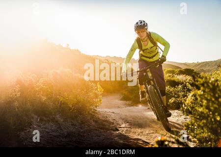 Weibliche Moutainbiker fahren auf Feldweg während Sonnenuntergang, Fort Ord National Monument Park, Monterey, Kalifornien, USA Stockfoto