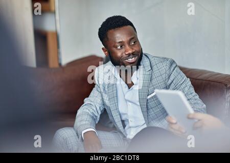 Porträt eines lächelnden Geschäftsmann sitzt auf der Couch und sieht Kollegen Stockfoto