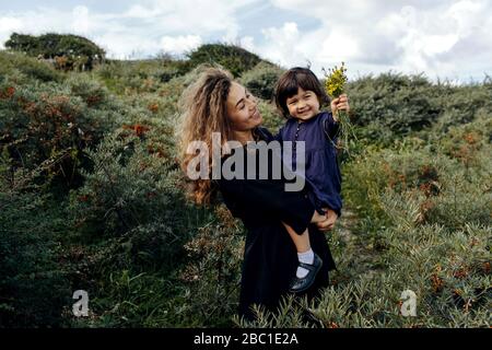 Glückliche Mutter und kleine Tochter mit gepflückten Blumen in der Natur, Den Haag, Niederlande Stockfoto