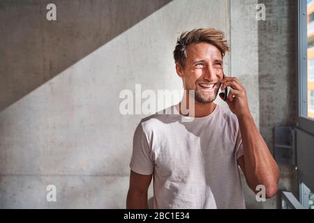 Fröhlicher junger Mann, der T-Shirt trägt und am Telefon telefoniert