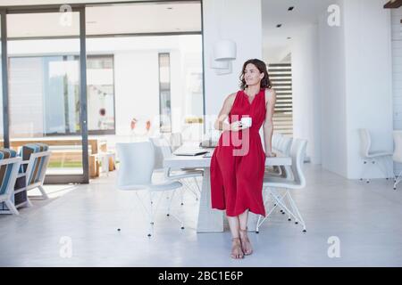 Portrait selbstbewusste Brunette-Frau im roten Kleid, die Kaffee im Speisesaal trinkt Stockfoto