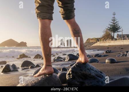 Beine eines Mannes, der auf Steinen am Strand steht, Sao Miguel Insel, Azoren, Portugal Stockfoto