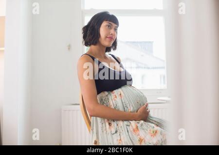 Nachdenkliche schwangere Frau, die Magen hält Stockfoto