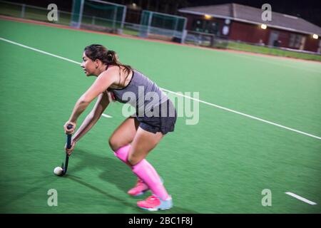 Festgestellte junge Feldhockeyspielerin, die nachts auf dem Feld spielt Stockfoto