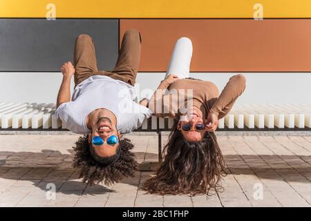 Pärchen mit Sonnenbrille, auf Bank entspannen, auf dem Rücken liegen, Köpfe hängen Stockfoto