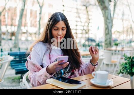 Junge Frau sitzt am Tisch im Freien und mit dem Smartphone Stockfoto