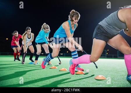 Junge Feldhockeyspielerinnen, die nachts Sportübung auf dem Feld üben Stockfoto