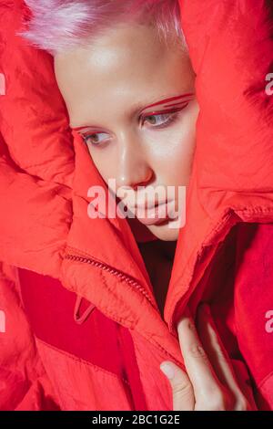 Porträt einer jungen Frau mit kurzen rosa Haaren trägt rote Jacke vor rotem Hintergrund Stockfoto