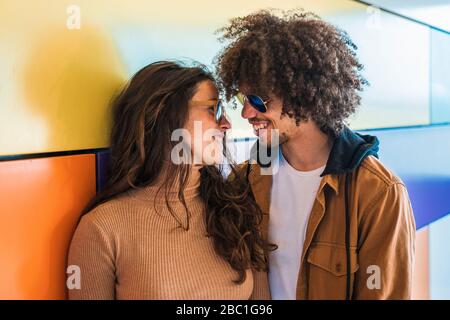 Liebevolles Paar lächelt sich vor einer bunten Wand an Stockfoto