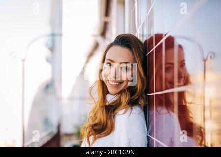 Porträt einer glücklichen jungen Frau, die sich gegen eine Fliesenwand lehnt
