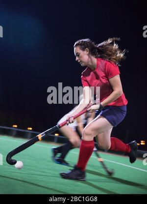 Festgestellte junge Feldhockeyspielerin, die nachts auf dem Feld spielt Stockfoto