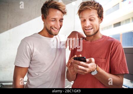 Zwei glückliche junge Männer teilen Smartphone Stockfoto