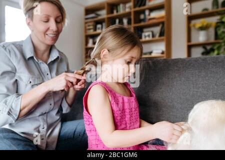 Mutter flechtete die Haare ihrer Tochter auf der Couch Stockfoto