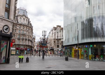 Ein menschenleerer Leicester Square im Zentrum Londons während des Ausbruchs des Corona-Virus. Zwei einsame Polizisten sind zu sehen. Stockfoto