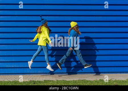 Zwei Teenager-Mädchen in passender Kleidung springen in der Luft vor blauem Hintergrund Stockfoto