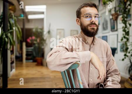 Junger Mann auf Stuhl sitzend, die Kamera skeptisch betrablickend Stockfoto