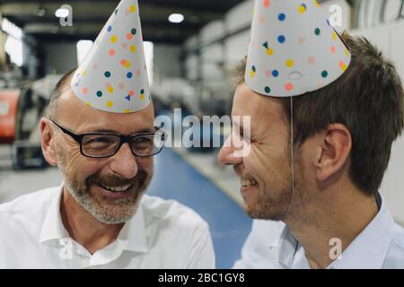 Porträt von zwei glücklichen Geschäftsleuten, die in einer Fabrik Partyhüte tragen Stockfoto