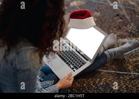 Frau mit Weihnachtsmann Hut auf der Suche nach Geschenken online, mit Laptop Stockfoto