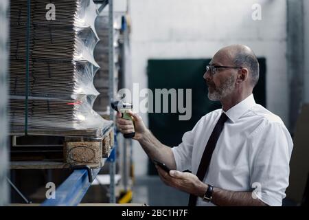 Mann mit Smartphone und Scanner im Fabriklager Stockfoto