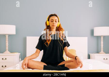 Junge Frau, die mit Kopfhörern zu Hause im Bett meditiert Stockfoto