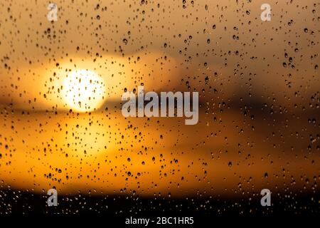 Bei Sonnenuntergang fällt Regen auf ein Fenster Stockfoto