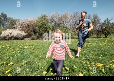 Kleines Mädchen und ihr Vater laufen im Frühling auf einer Wiese Stockfoto