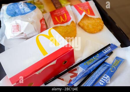 Essen bei McDonald's. Eine Reihe von Frühstücksprodukten auf einem Tablett Dranik, einrosafarbene Zuckerpakete, Burger, Servietten, Strohhalme. Stockfoto